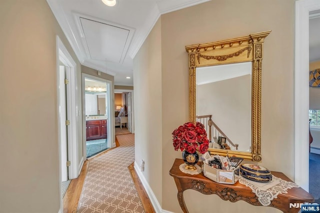 hallway with attic access, wood finished floors, baseboards, and ornamental molding