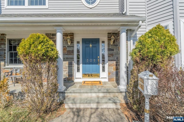 property entrance featuring covered porch, stone siding, and roof with shingles