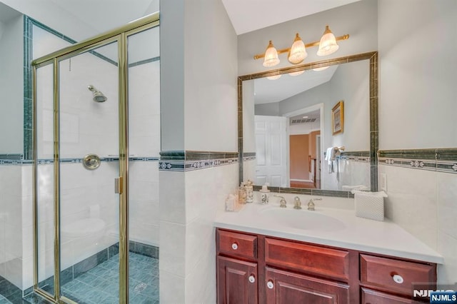 bathroom featuring wainscoting, a stall shower, tile walls, and vanity