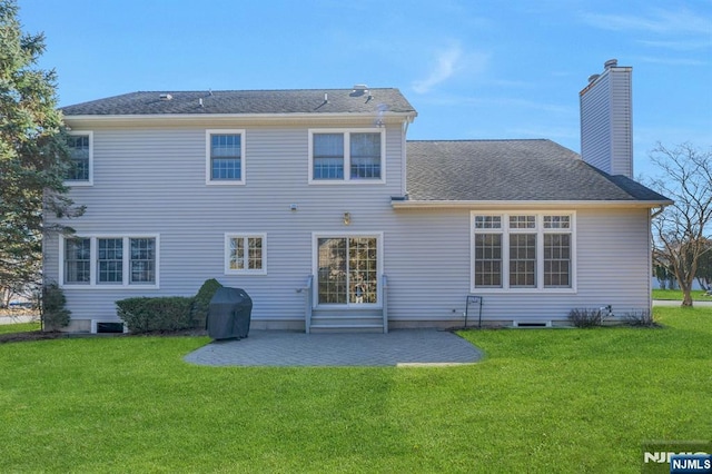 rear view of property with a patio, a lawn, roof with shingles, and a chimney