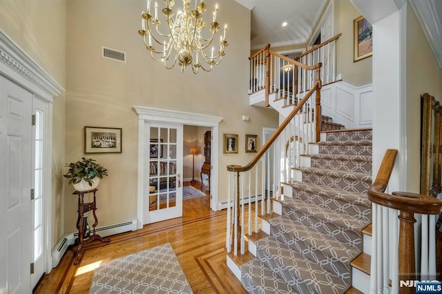 entrance foyer with visible vents, ornamental molding, wood finished floors, a high ceiling, and baseboard heating