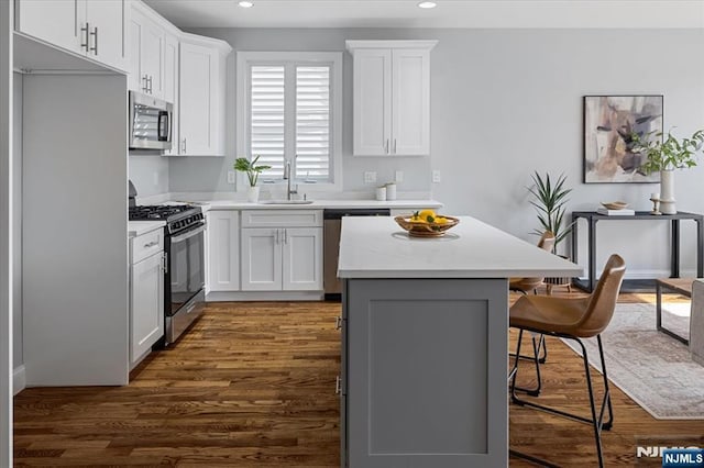 kitchen featuring a breakfast bar, appliances with stainless steel finishes, dark wood-type flooring, a sink, and a kitchen island