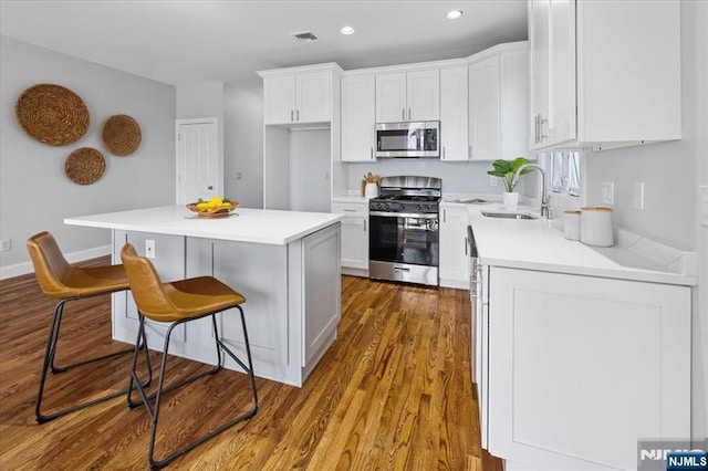 kitchen with stainless steel appliances, a kitchen island, a sink, white cabinets, and a kitchen bar