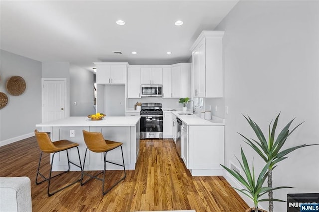 kitchen featuring a breakfast bar, a sink, white cabinetry, light countertops, and appliances with stainless steel finishes