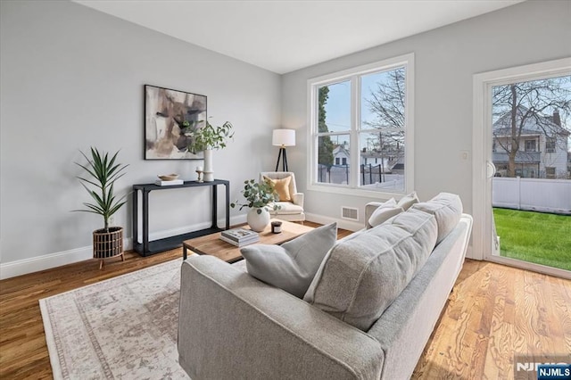 living area with a wealth of natural light, wood finished floors, visible vents, and baseboards