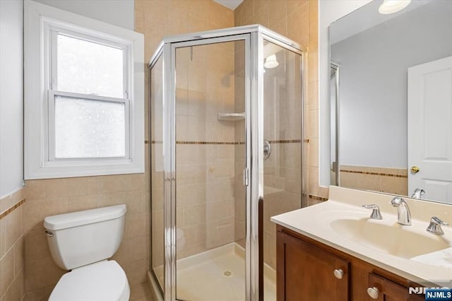 bathroom with toilet, a stall shower, vanity, and tile walls