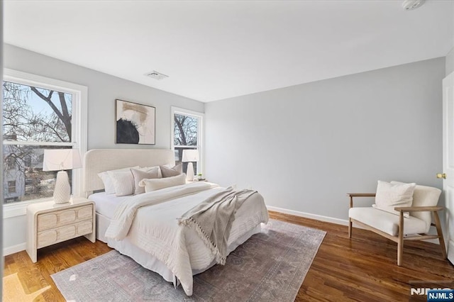 bedroom with baseboards, multiple windows, visible vents, and wood finished floors