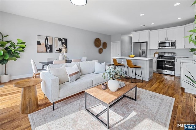 living area with baseboards, wood finished floors, and recessed lighting