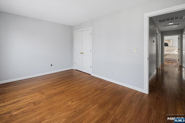 empty room with attic access, baseboards, and dark wood finished floors