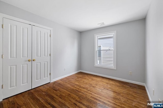 unfurnished bedroom featuring dark wood-style floors, baseboards, visible vents, and a closet