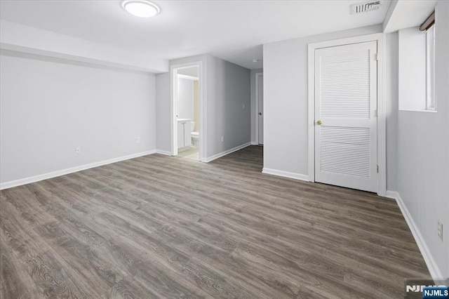 unfurnished bedroom featuring visible vents, ensuite bathroom, baseboards, and wood finished floors