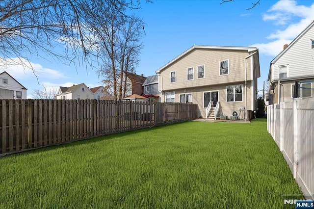 back of house with entry steps, a fenced backyard, and a yard