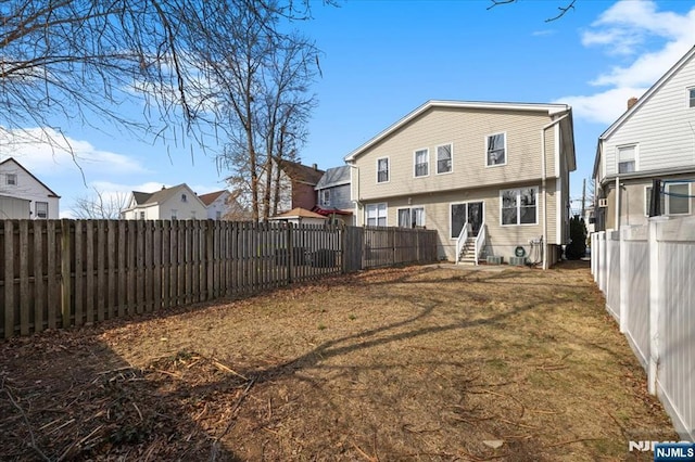 back of property with entry steps, a fenced backyard, and a yard