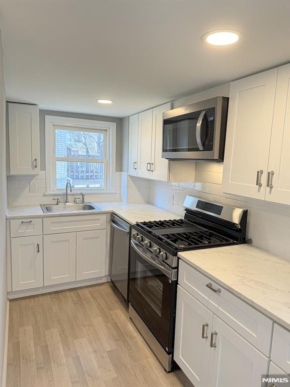 kitchen with appliances with stainless steel finishes, a sink, light wood-style flooring, and white cabinets