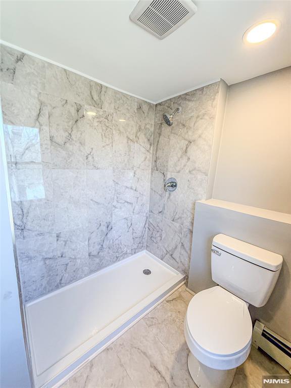 bathroom featuring toilet, visible vents, marble finish floor, baseboard heating, and a tile shower