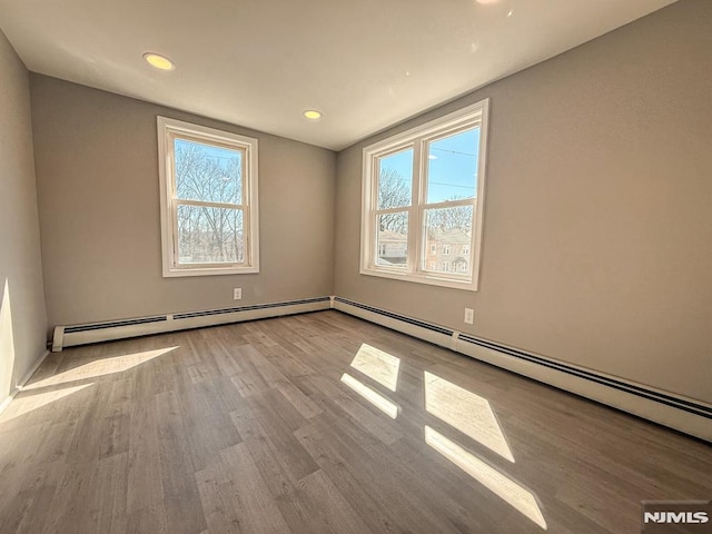 unfurnished room featuring a baseboard radiator, wood finished floors, and recessed lighting