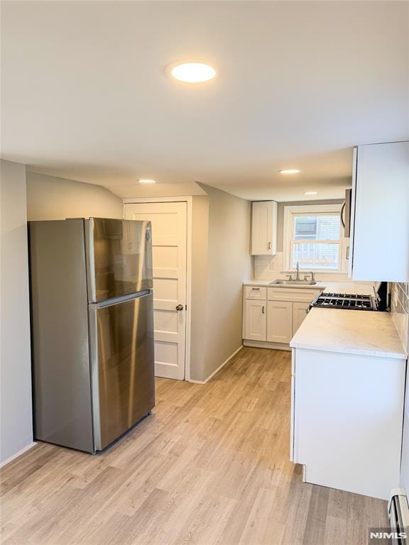 kitchen with light countertops, baseboard heating, appliances with stainless steel finishes, a sink, and light wood-type flooring