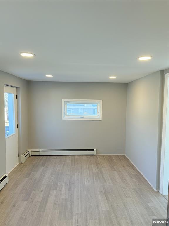 empty room featuring a baseboard heating unit, recessed lighting, and light wood-style floors