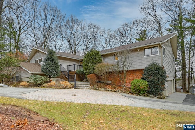 view of front facade featuring brick siding, driveway, an attached garage, and stairs