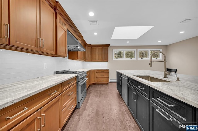 kitchen with light stone counters, a skylight, appliances with stainless steel finishes, a sink, and exhaust hood