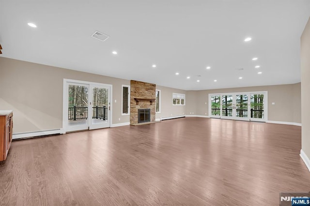 unfurnished living room featuring a stone fireplace, a baseboard radiator, wood finished floors, and visible vents