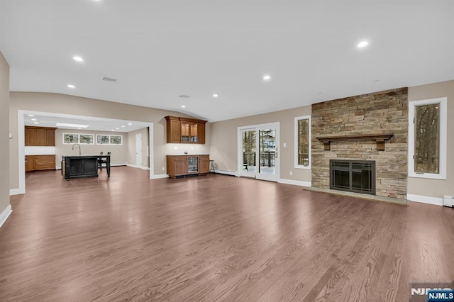 unfurnished living room with lofted ceiling, a stone fireplace, dark wood finished floors, and baseboards