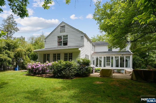 rear view of property featuring a sunroom, a patio, and a lawn