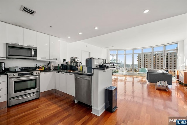 kitchen featuring wood finished floors, visible vents, a sink, stainless steel appliances, and dark countertops