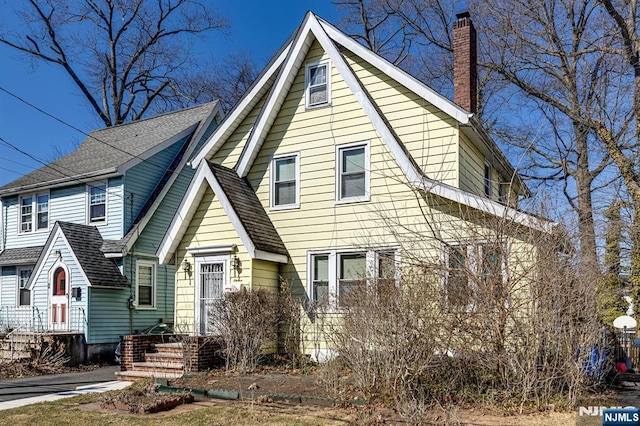 view of front facade featuring roof with shingles and a chimney