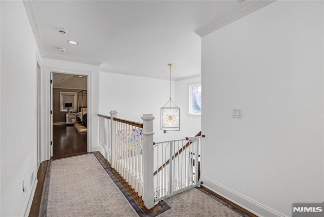 corridor featuring a notable chandelier, wood finished floors, an upstairs landing, baseboards, and crown molding