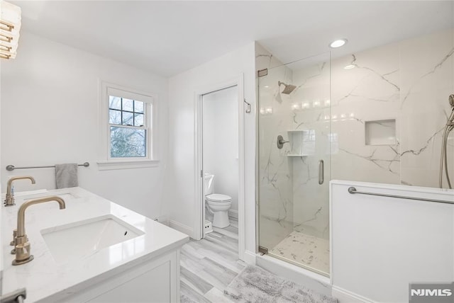 bathroom featuring toilet, recessed lighting, a sink, a marble finish shower, and double vanity