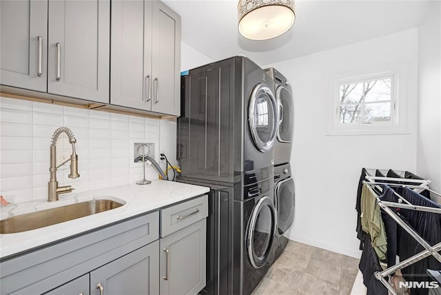 laundry room featuring stacked washer / dryer, a sink, cabinet space, and baseboards