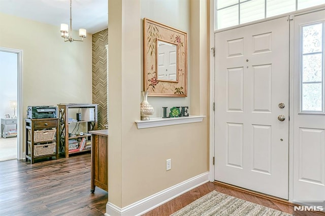 foyer entrance with a notable chandelier, dark wood-style flooring, and baseboards