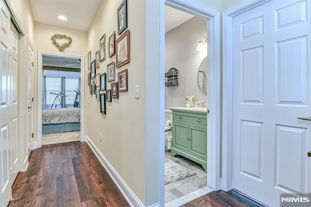 hall with dark wood-style floors, baseboards, and a sink