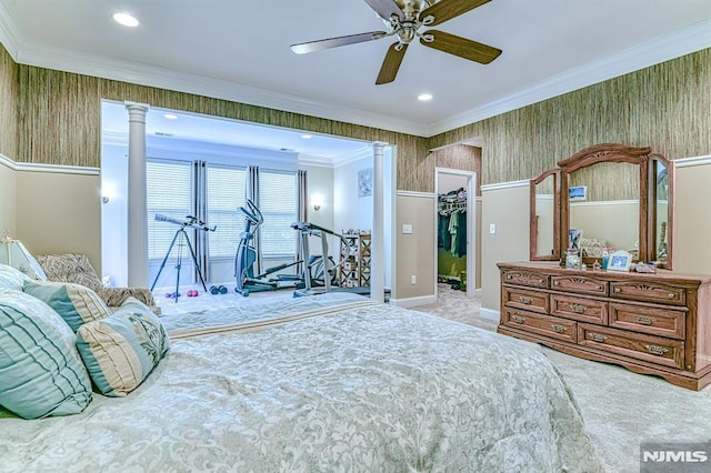 carpeted bedroom featuring crown molding, wallpapered walls, a walk in closet, and ornate columns