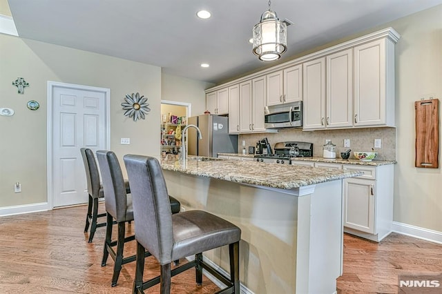 kitchen with appliances with stainless steel finishes, light wood-style flooring, a breakfast bar, and tasteful backsplash