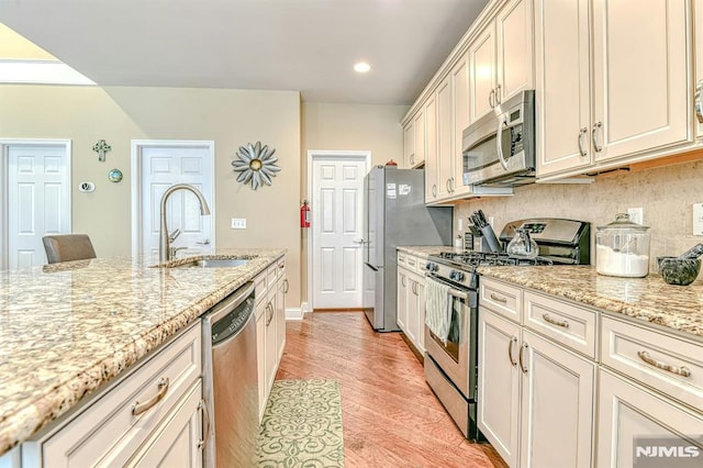 kitchen featuring a sink, appliances with stainless steel finishes, light wood-type flooring, backsplash, and light stone countertops