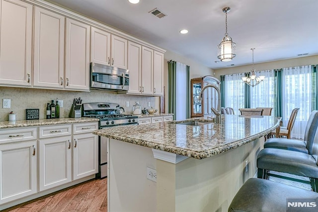 kitchen with stainless steel appliances, a sink, visible vents, a kitchen breakfast bar, and tasteful backsplash