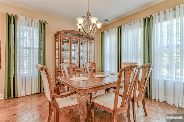 dining space featuring a chandelier, light wood-style flooring, visible vents, and baseboards