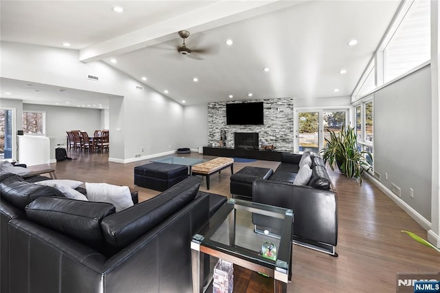 living room with a stone fireplace, beamed ceiling, wood finished floors, and baseboards