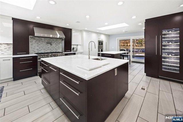 kitchen with wall chimney exhaust hood, modern cabinets, and a center island with sink