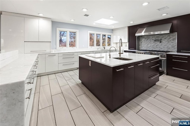 kitchen featuring wall chimney range hood, modern cabinets, a sink, and stainless steel stove