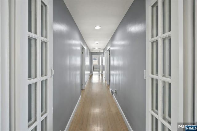 hall with attic access, wood-type flooring, and baseboards