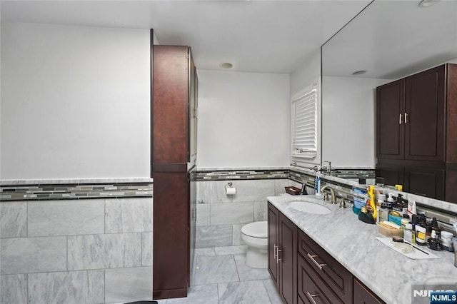 full bath featuring tile walls, wainscoting, vanity, and toilet