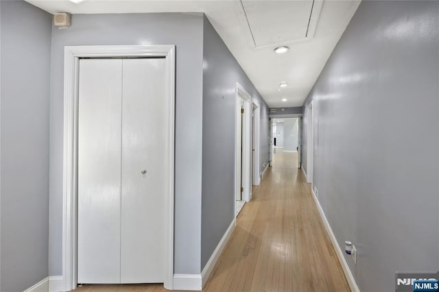 corridor featuring attic access, baseboards, and light wood-style flooring