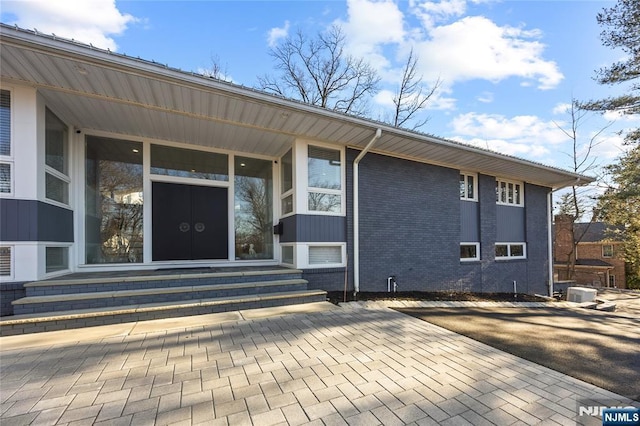 view of exterior entry featuring cooling unit and brick siding