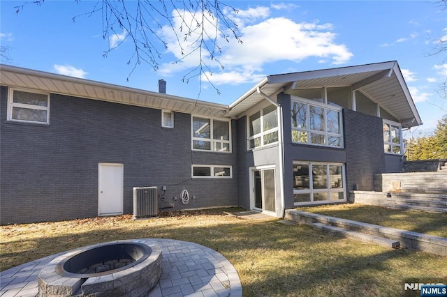 back of house featuring central air condition unit, a chimney, a fire pit, and brick siding