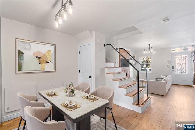 dining room featuring light wood-style floors, an inviting chandelier, baseboards, and stairs