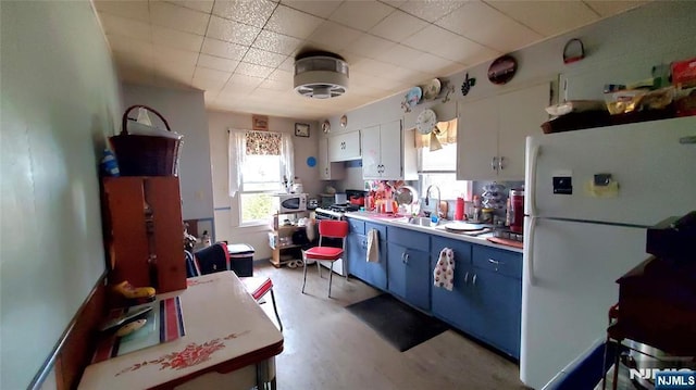 kitchen featuring a wealth of natural light, blue cabinetry, freestanding refrigerator, and a sink