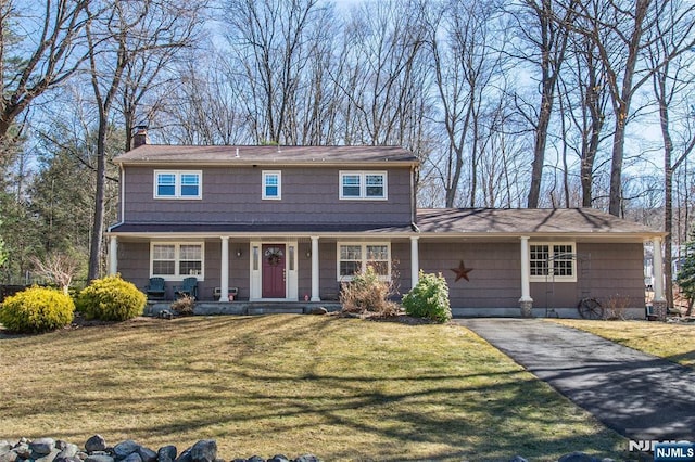 view of front of property with aphalt driveway, a porch, a chimney, and a front lawn